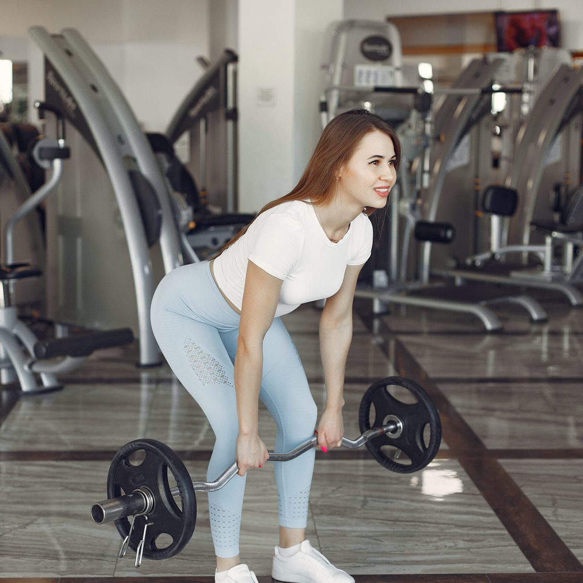 A beautiful girl is engaged in a gym with a barbell back fat