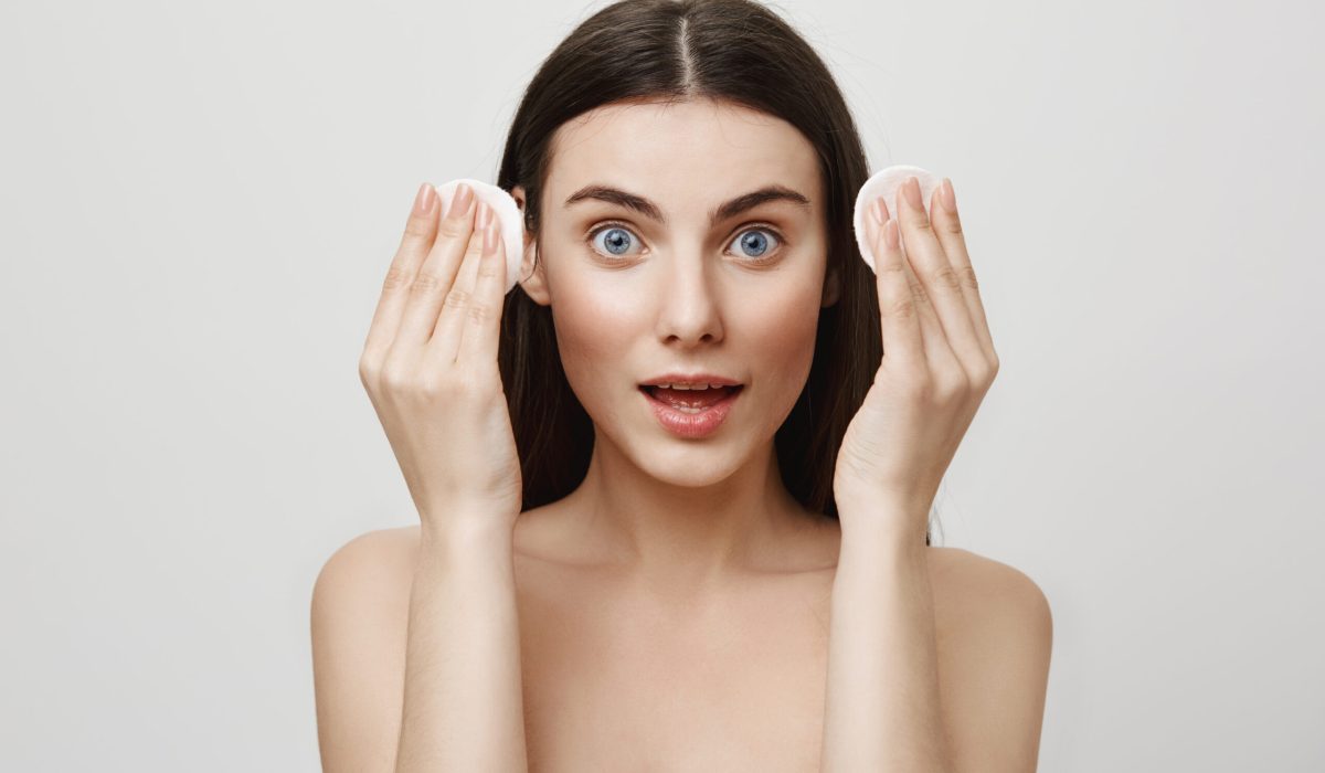 Beauty and cosmetological procedure concept. Portrait of good-looking expressive woman holding cotton pads in hands, getting ready to wipe off mascara and makeup while standing over gray wall eye skin