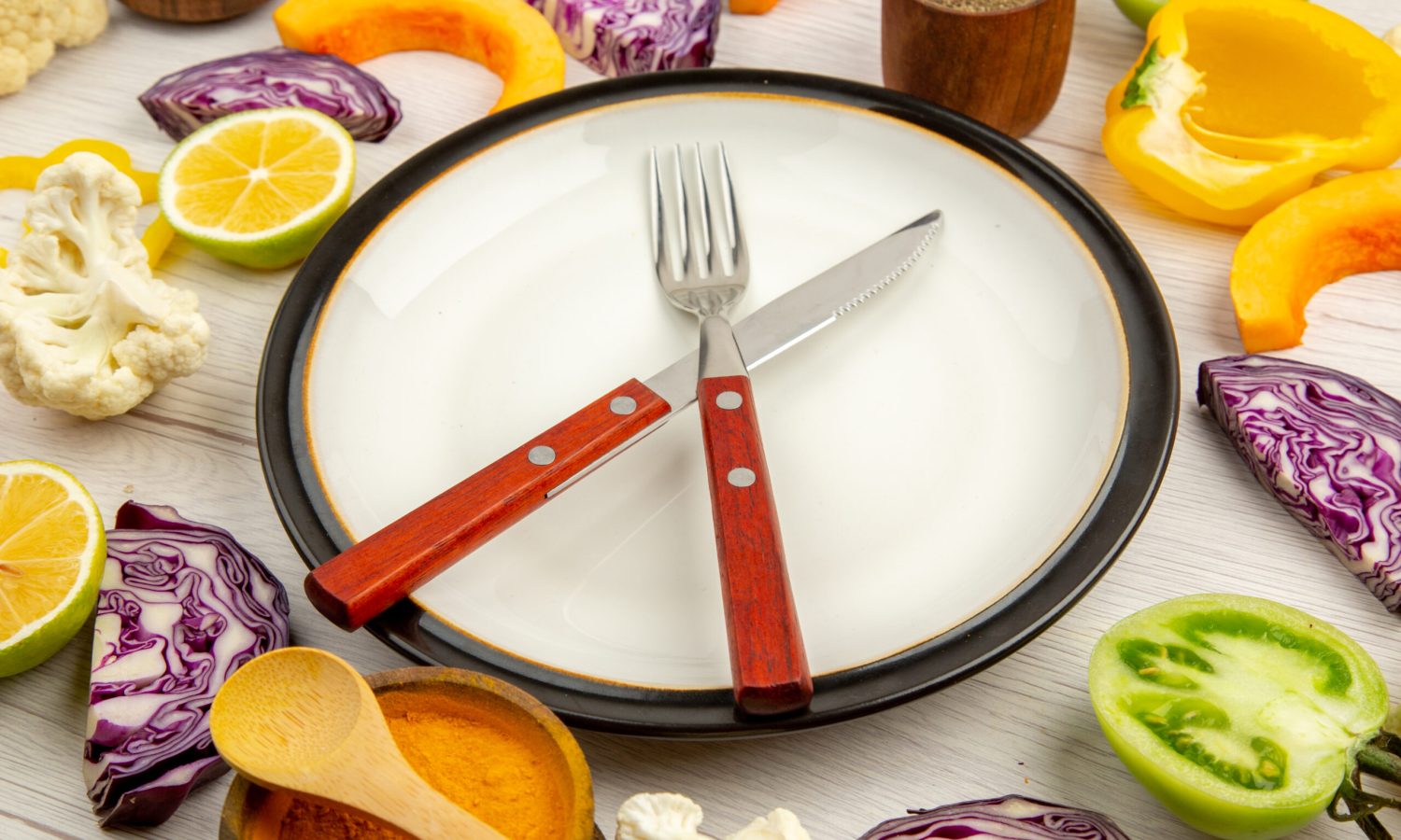 bottom-view-cut-vegetables-pumpkin-red-cabbage-lemon-green-tomatoes-cauliflower-yellow-bell-peppers-crossed-knife-fork-plate-spices-small-bowls-table weight control