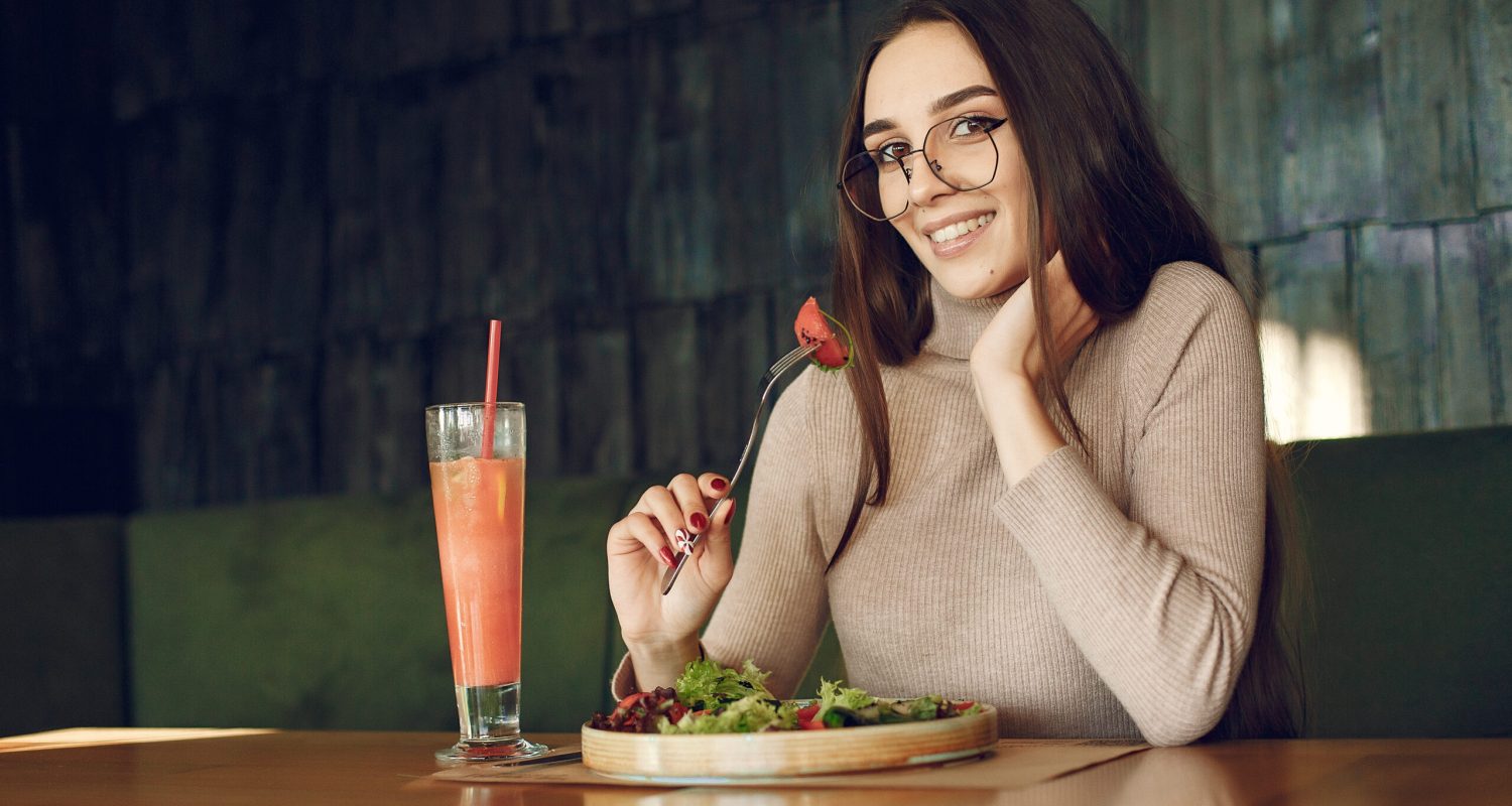 Elegant woman sitting at the table with cocktail and salad Girl in a cafe. Woman in a brown sweater. Lady with salad and cocktail.