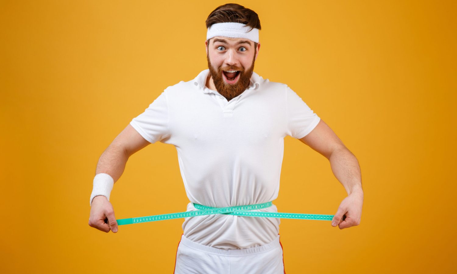 Happy bearded fitness man measuring his waist with tape body fat